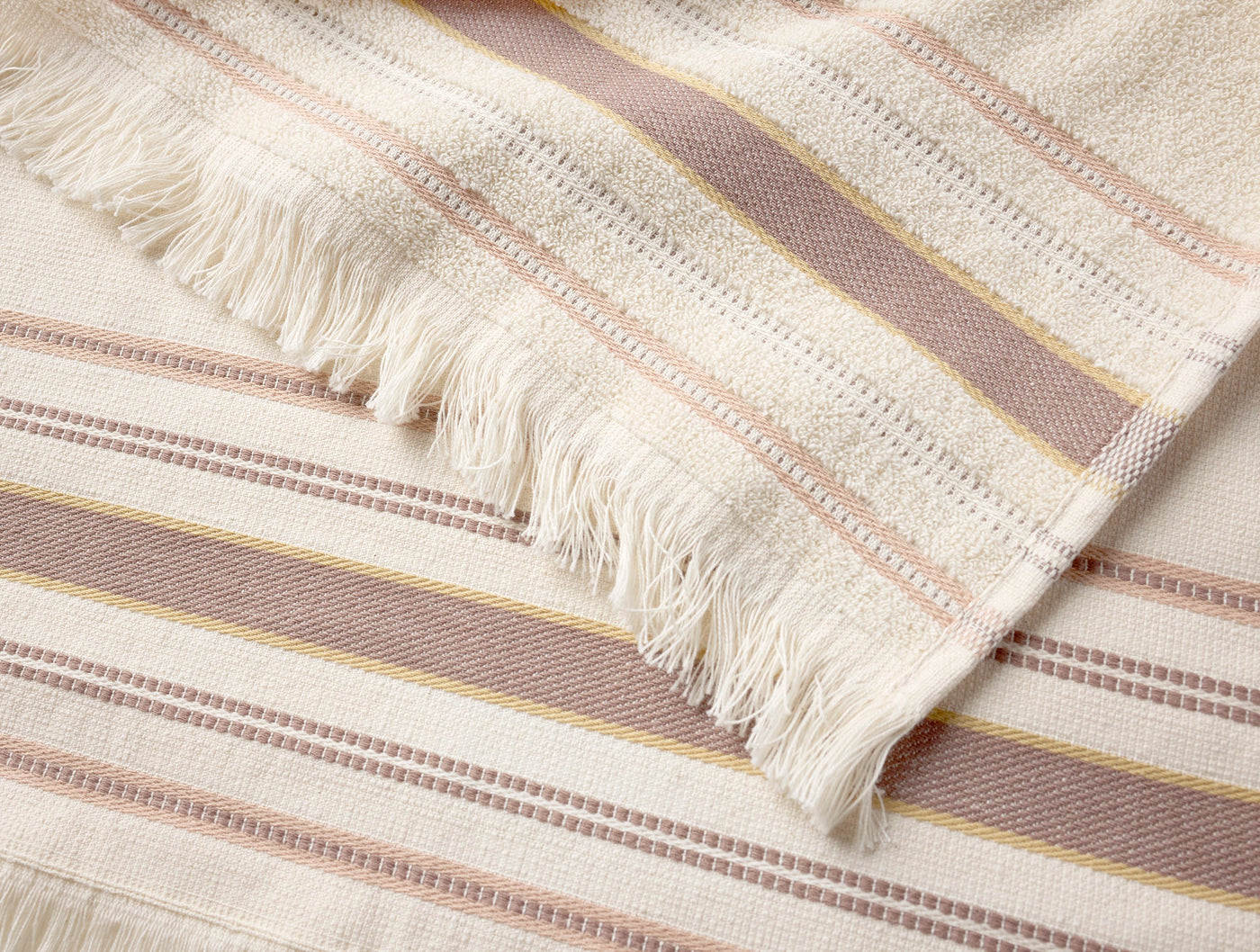 Close-up of Coyuchi Aptos hand towel fringe edge with rose, blush, and gold stripes on ivory.