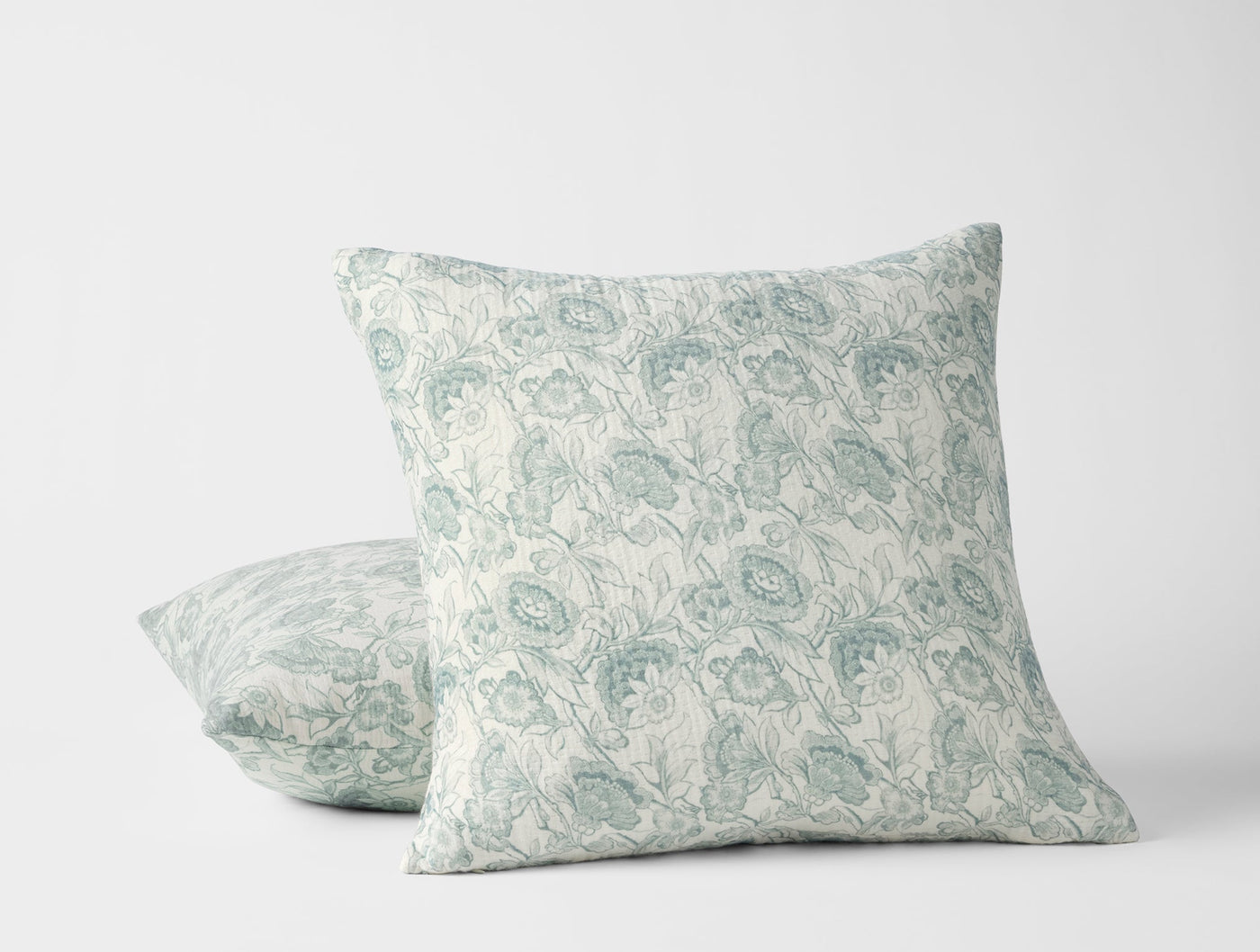 Two Coyuchi Balboa Matelassé pillows, ivory with sage floral print, stacked at an angle.