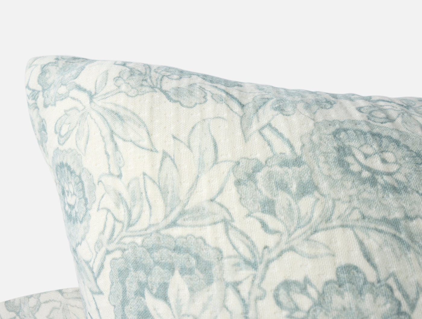 Close-up corner view of Coyuchi Balboa matelasse pillow in sage floral print on ivory.