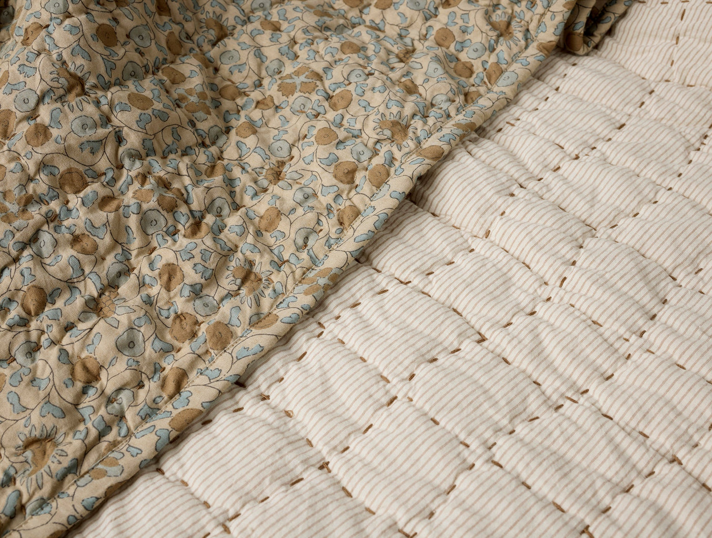 Close-up of Coyuchi Blossom quilt reverse, showing stripe and floral block-print sides.