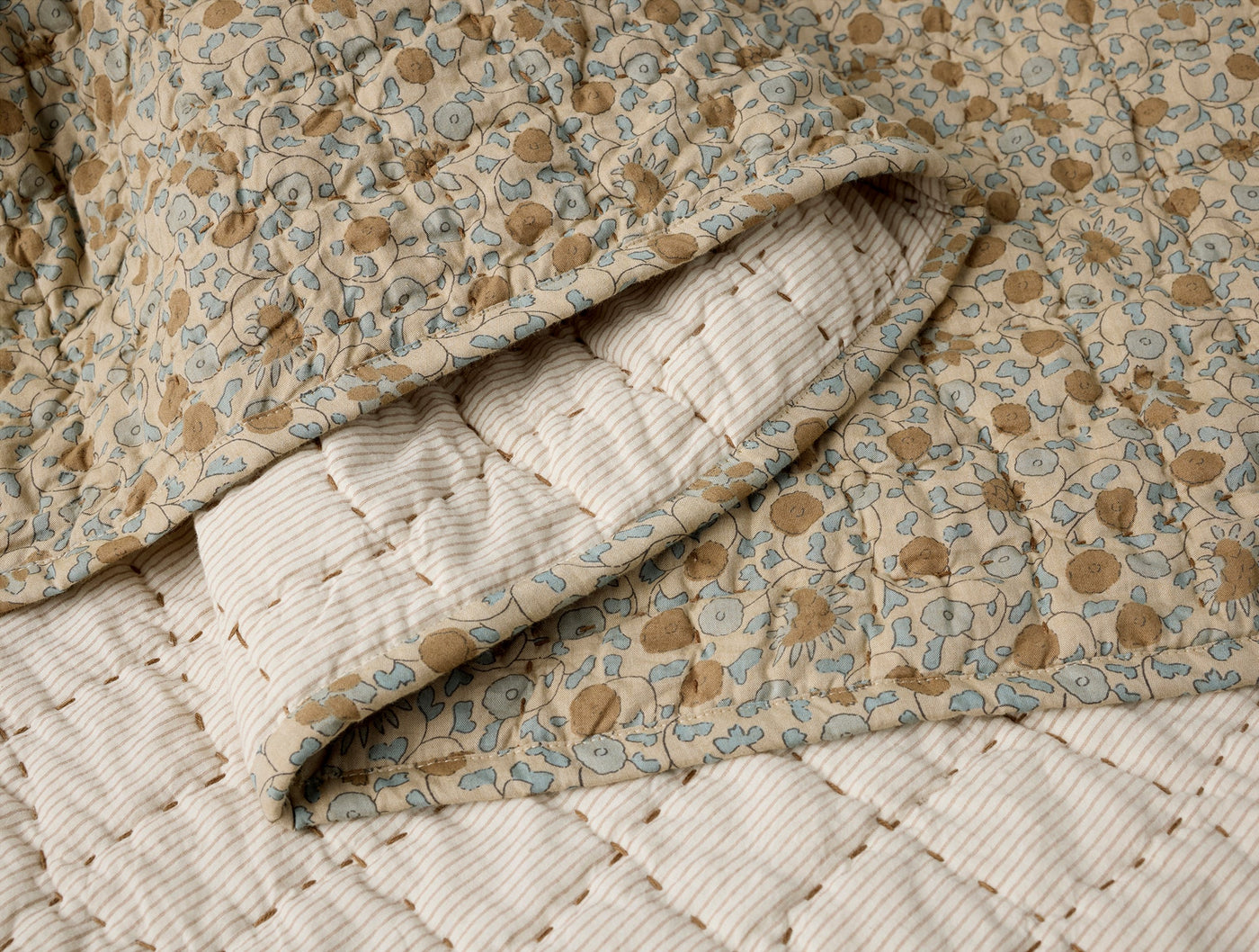 Close-up of Coyuchi Blossom quilt folded back, showing floral print exterior and striped interior lining.