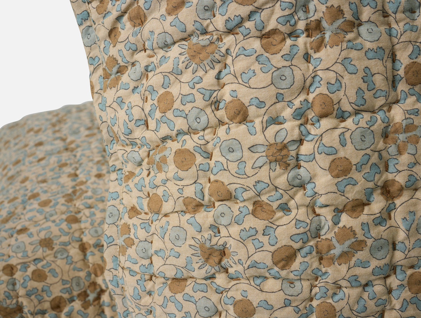 Close-up of Coyuchi Blossom Handstitched sham, ivory with blue and tan floral print, quilted detail.