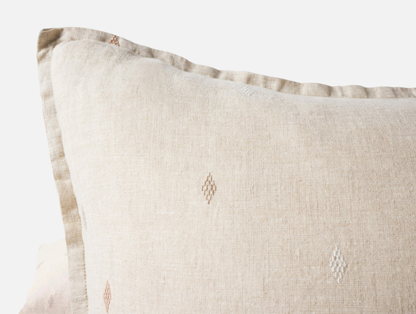 Close-up of natural linen pillow corner with diamond embroidery detail and flanged edge.