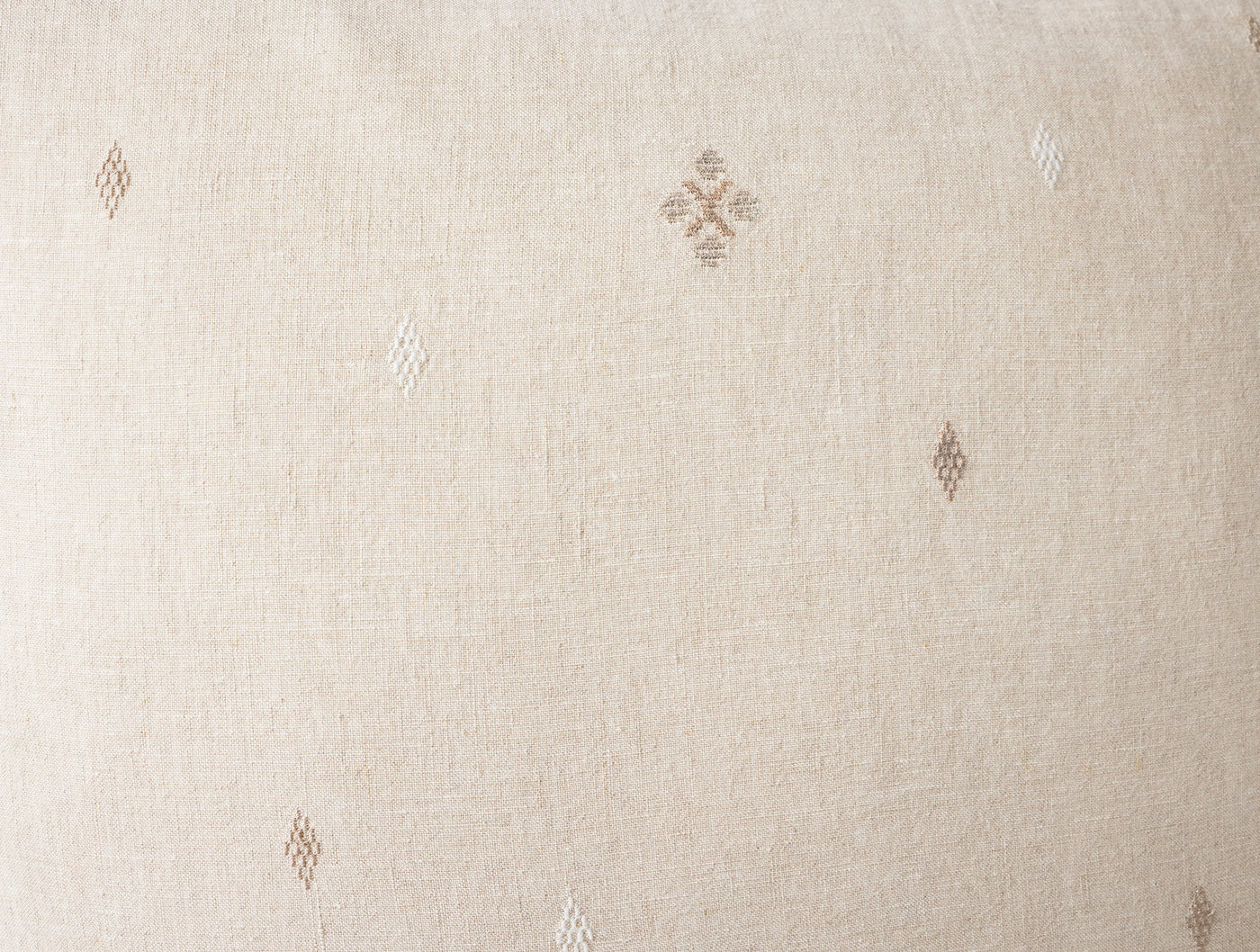 Close-up of ivory linen fabric with scattered taupe diamond and cross embroidered motifs.