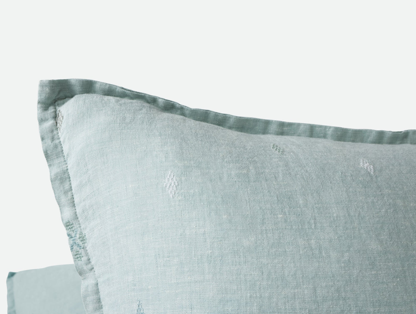 Close-up of Coyuchi Cambria pillow corner showing seafoam linen weave and subtle embroidered motifs.