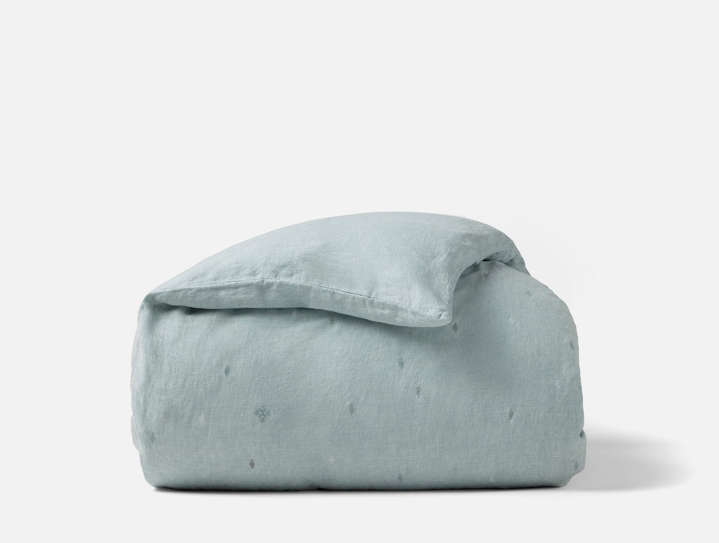 Cambria duvet cover folded compactly, showing sage linen with subtle embroidered dot detail.