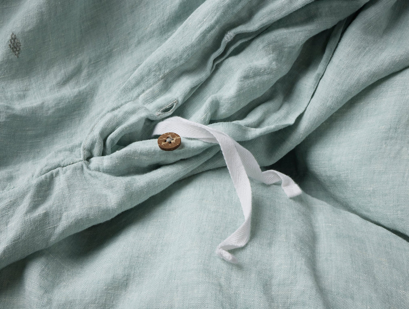 Close-up of sage linen duvet cover interior tie and coconut shell button closure detail.