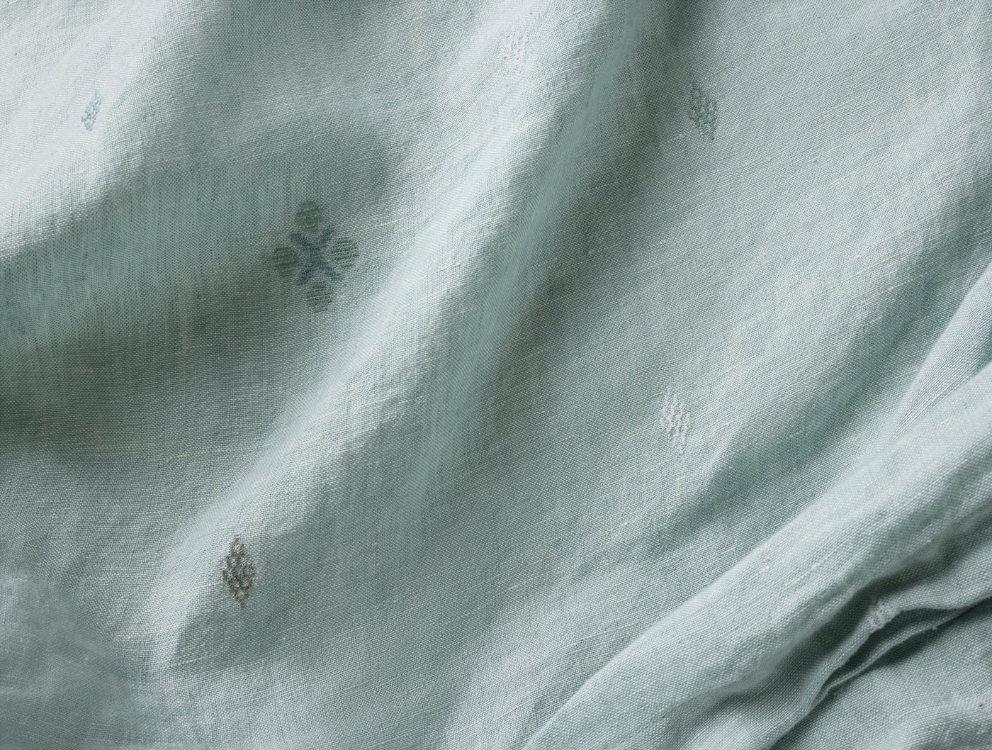 Close-up of sage green linen fabric with small embroidered diamond motifs and natural drape.