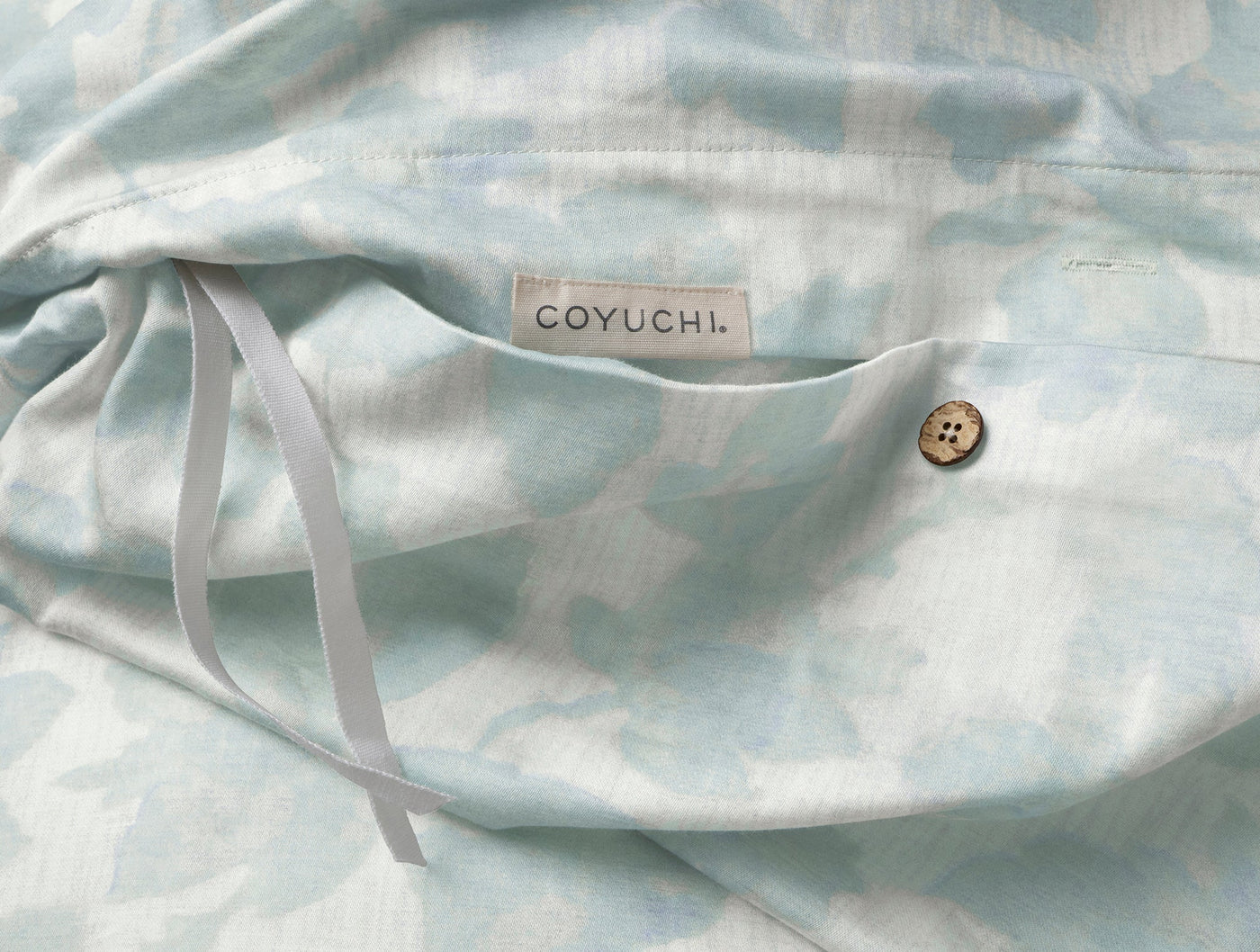 Close-up of Coyuchi duvet cover corner with button closure and tie, aqua floral print.