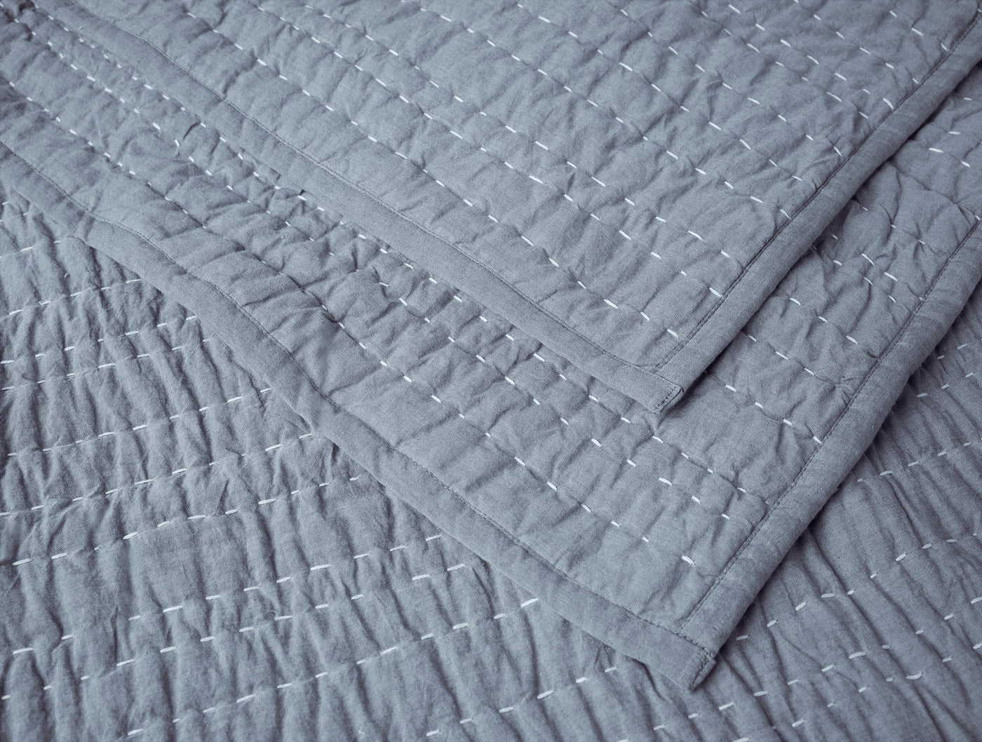 Close-up of Coyuchi Channel Handstitched quilt corner, slate blue with white hand-stitched channel detail.
