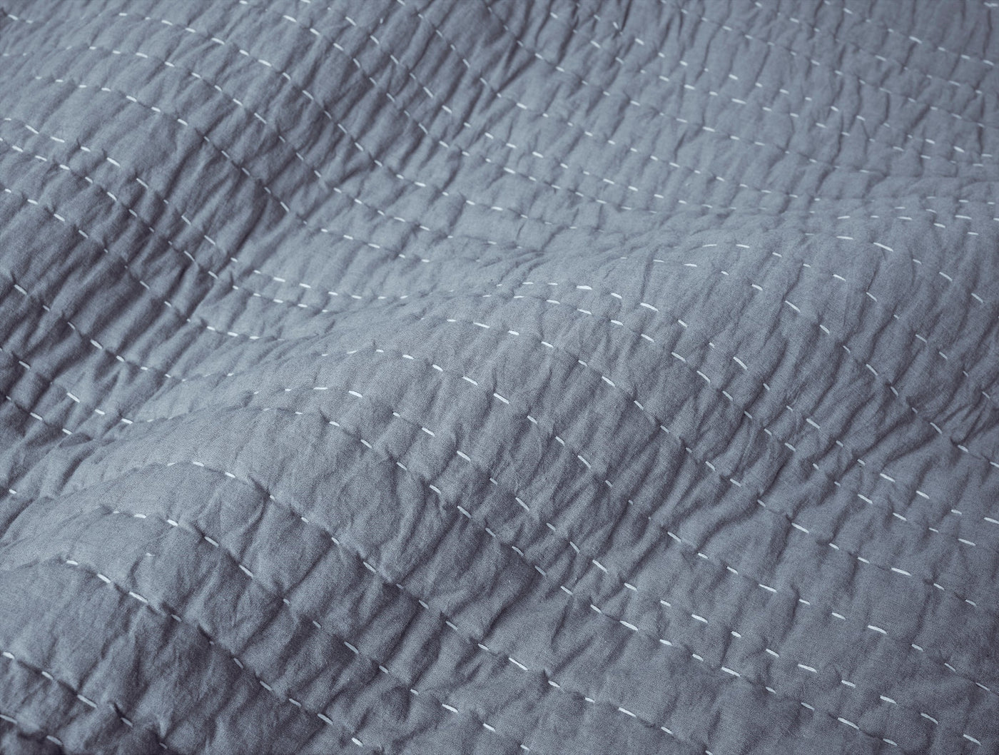 Close-up of slate blue Coyuchi Channel Handstitched quilt showing white running stitch detail.