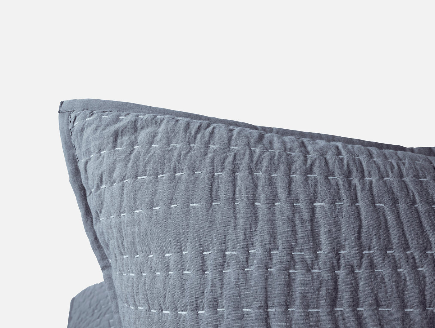 Close-up of slate blue linen sham corner with white hand-stitched channel quilting detail.