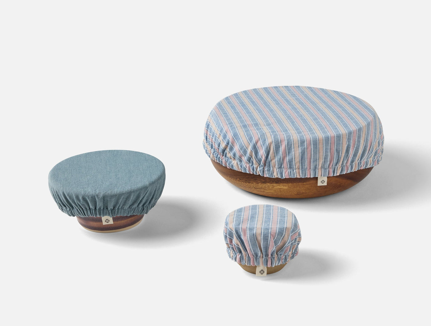 Three Coyuchi Conserve bowl covers in blue stripe linen, shown on wooden bowls in small, medium, large sizes.