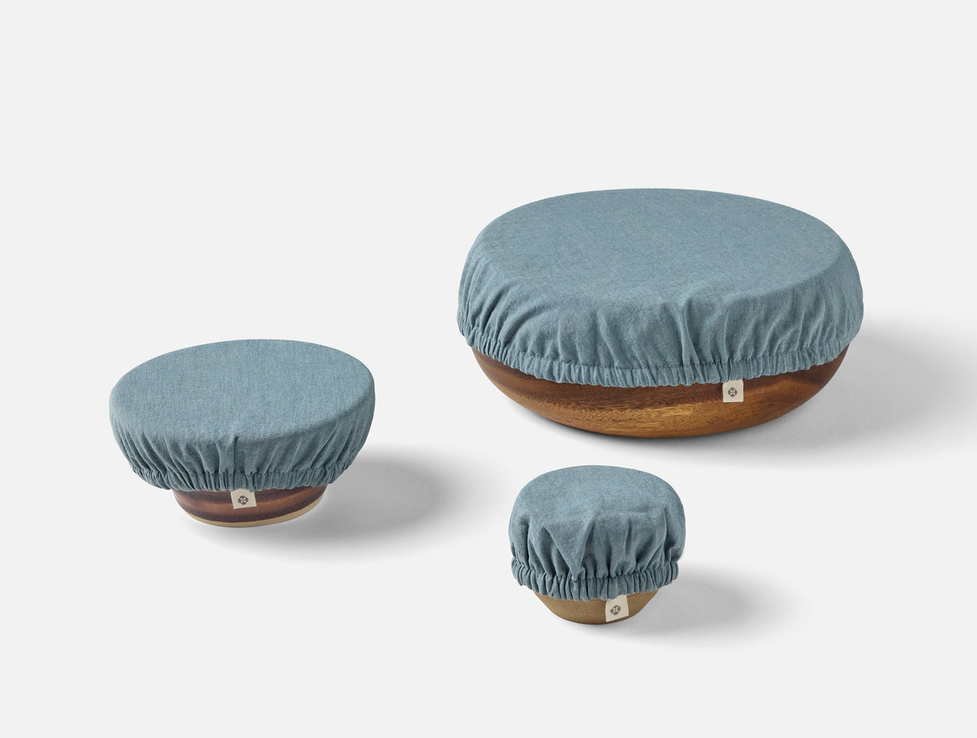 Three Coyuchi Conserve bowl covers in slate blue linen, sized small to large on wooden bowls.