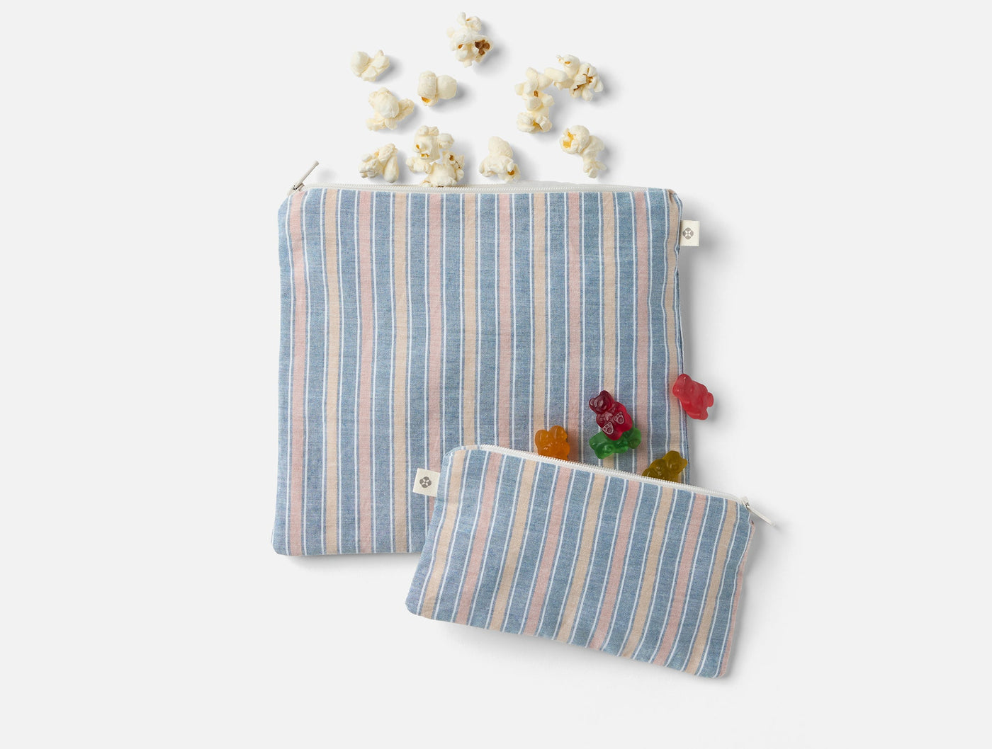 Two Coyuchi Conserve linen snack bags in blue stripe, styled with popcorn and gummy bears.