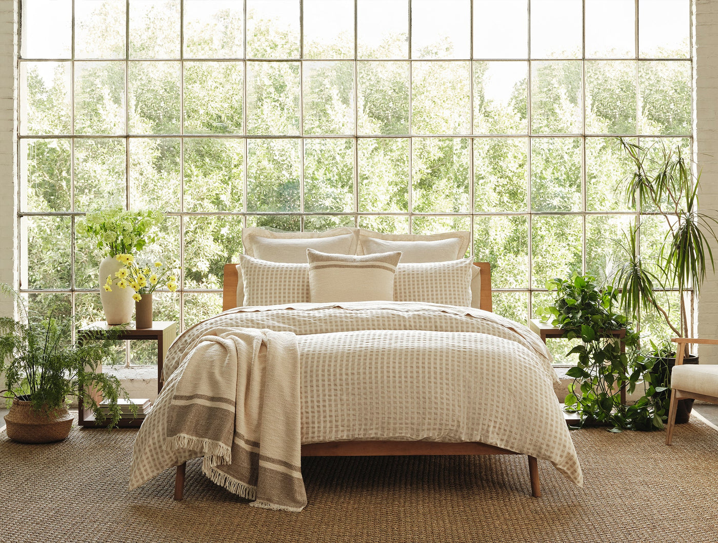 Pampas throw draped over a made bed in a plant-filled room with large windows.