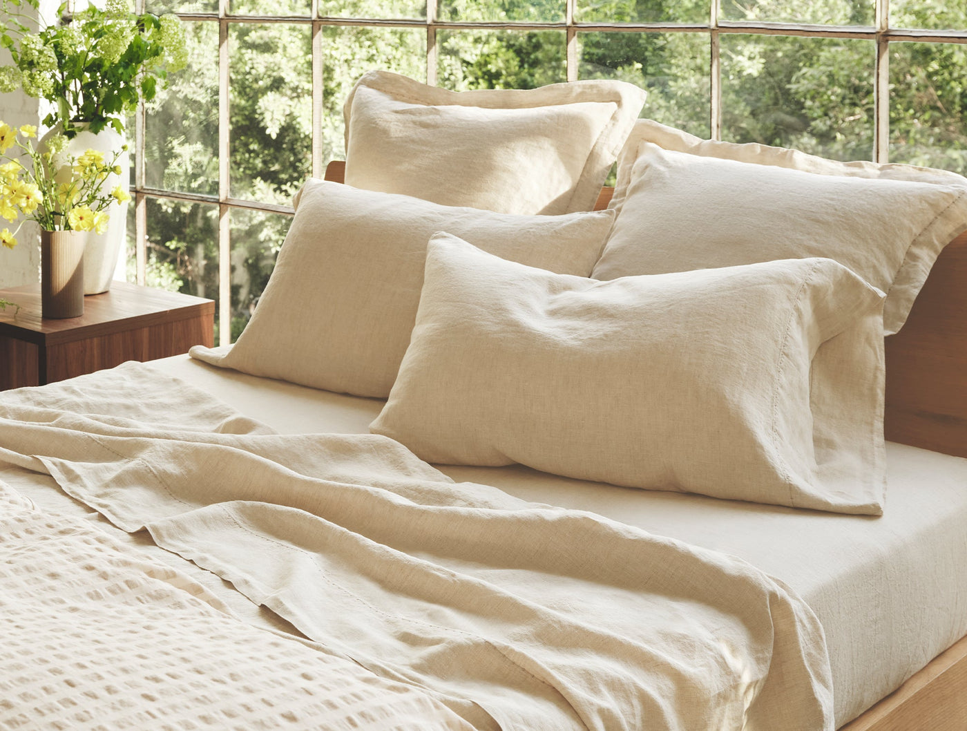 Close-up of Coyuchi Relaxed Linen sheet set in natural, styled on a sunlit bed with layered pillows.