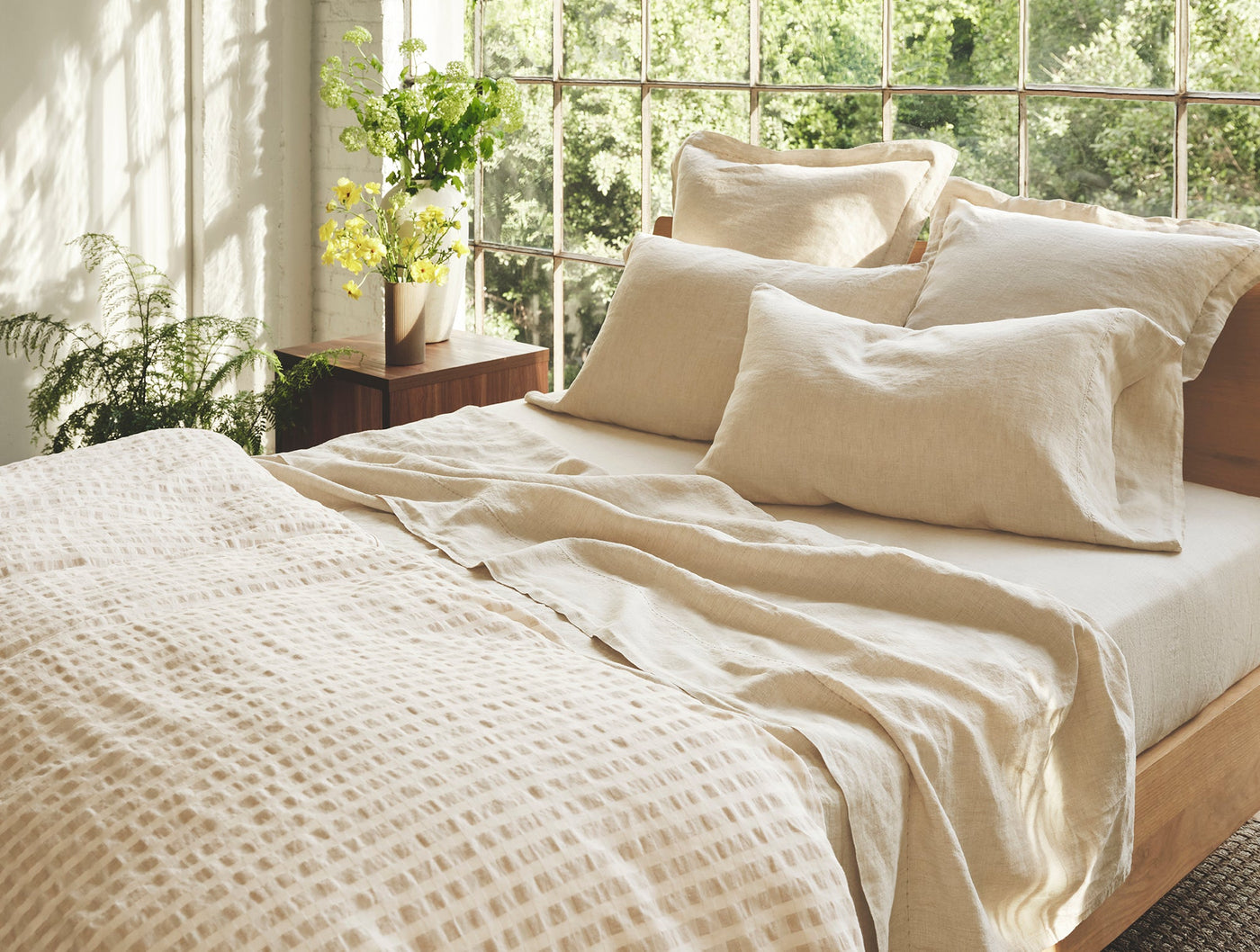 Ivory linen pillow shams styled on a sunlit bed with matching duvet and botanical backdrop.