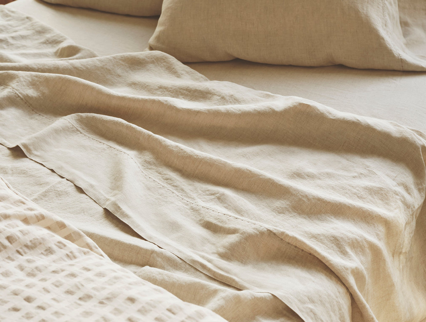 Close-up of draped oatmeal linen sheeting with natural texture and soft folds.