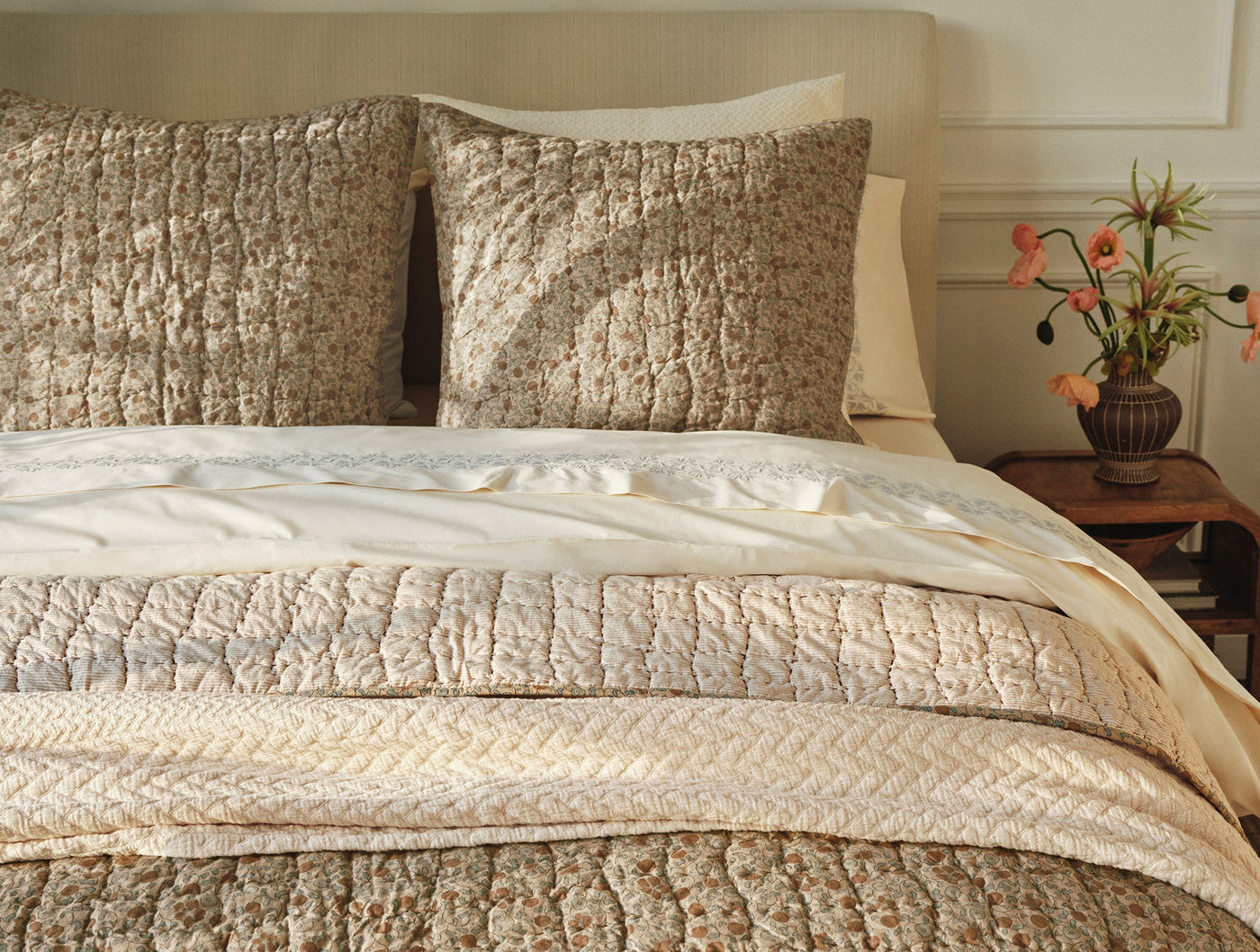 Quilt folded at foot of bed with matching shams, showing ivory and taupe floral pattern.