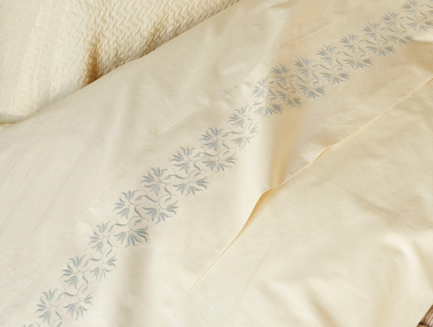 Close-up of ivory percale sheet hem with delicate blue floral embroidery border.