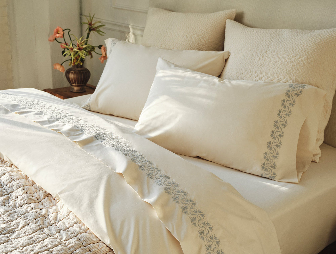 Ivory percale sheet set with grey floral embroidered border, styled on a made bed.