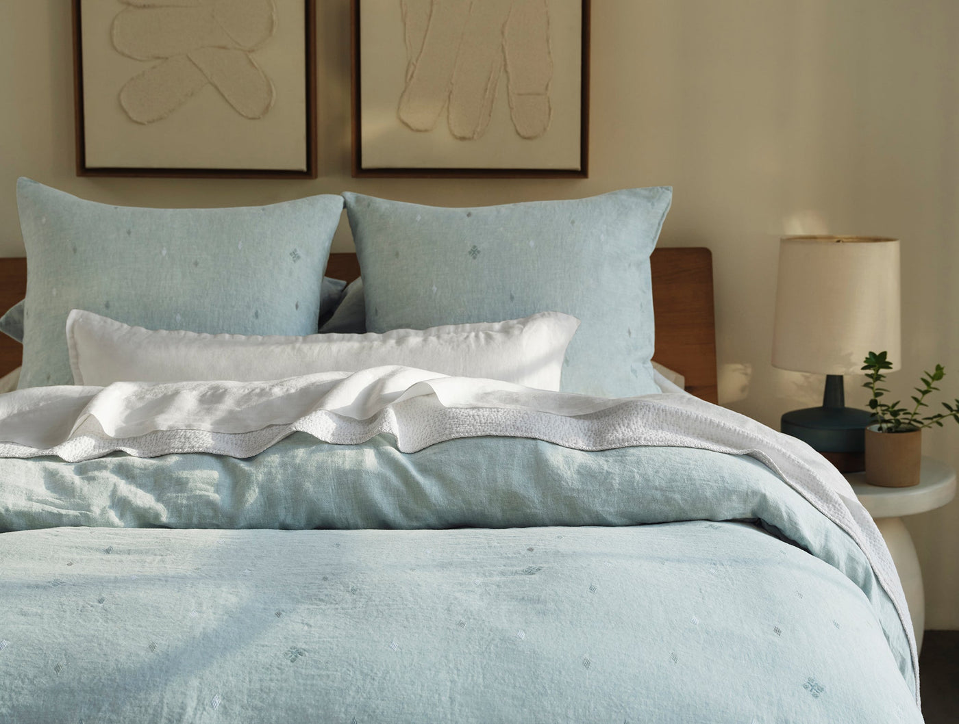 Pale blue embroidered linen shams styled on a made bed with layered white bedding.