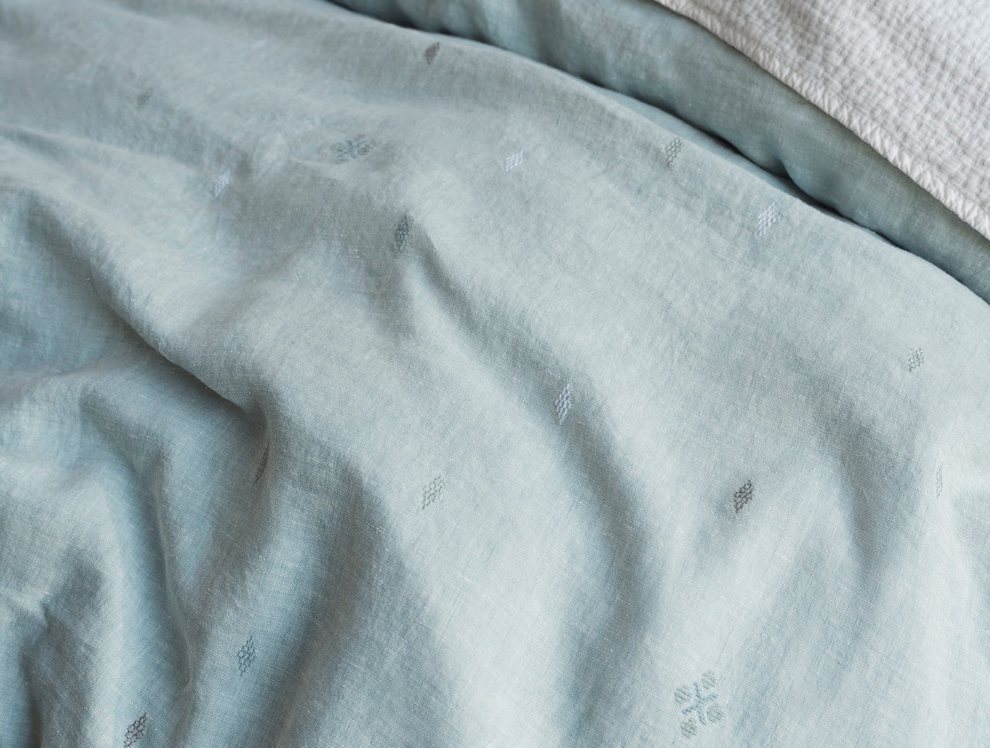 Close-up of Coyuchi Cambria duvet in mist blue, showing embroidered motifs on draped linen.