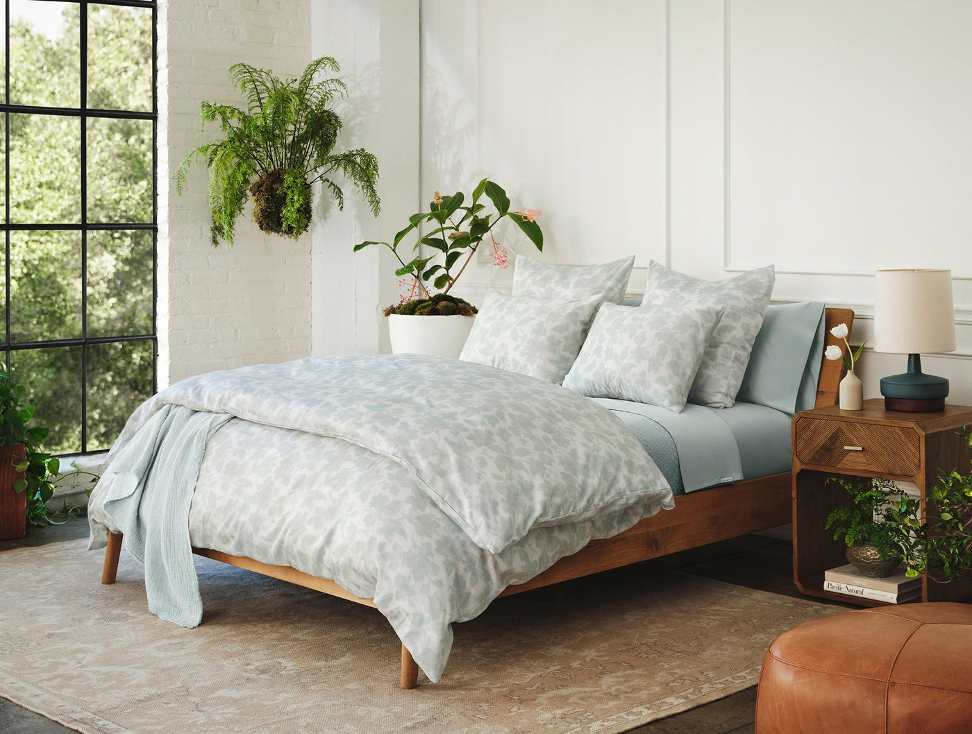 Coyuchi Camellia Print duvet cover styled on bed with sage flat sheet, surrounded by plants.
