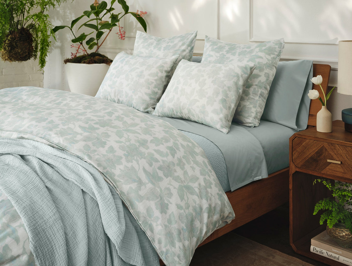 Camellia Print sham styled on a made bed with sage floral duvet and muted blue-green sheets.