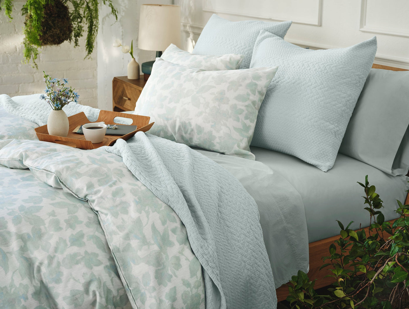 Sage green floral print sham styled with matelassé coverlet and solid shams on a made bed.