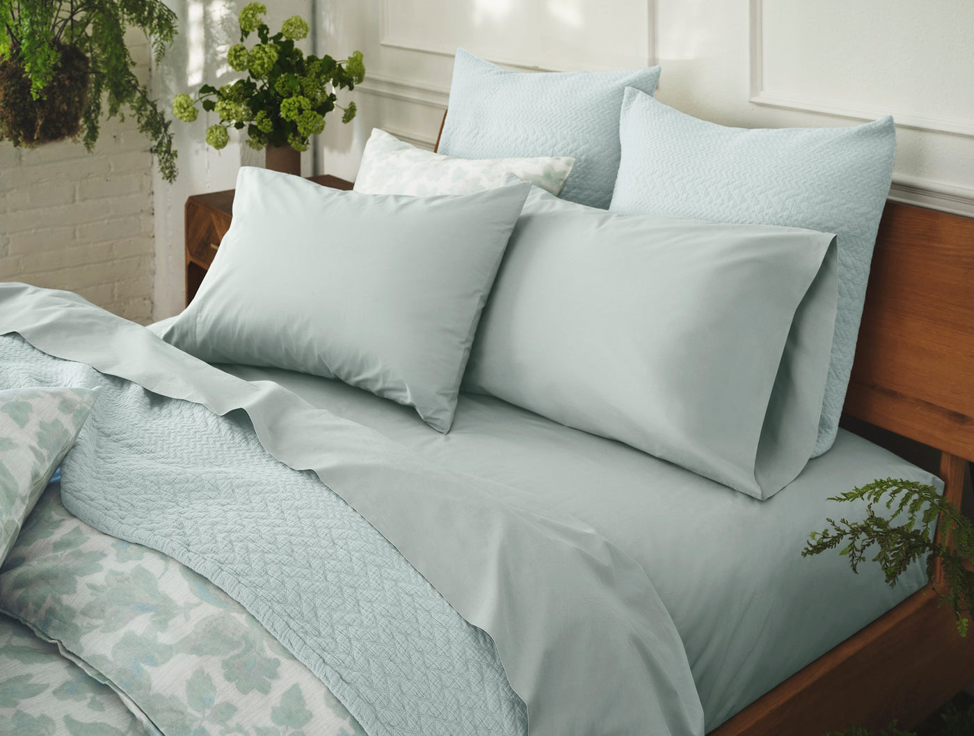 Sage green matelasse pillow shams stacked on a made bed with matching bedding.