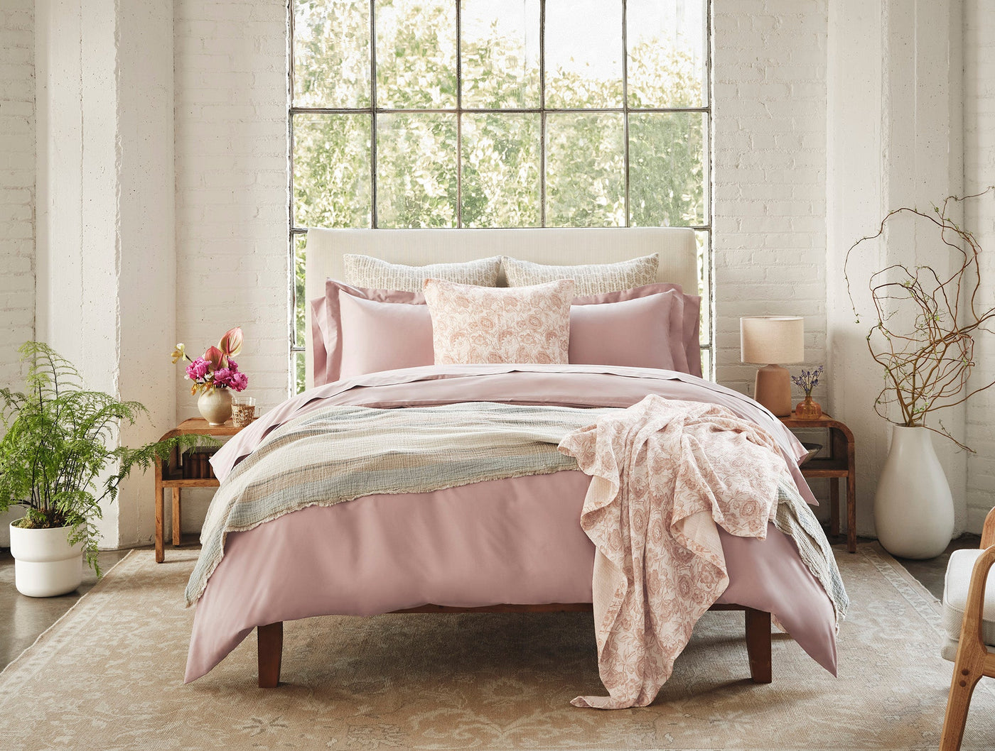 Blush pink floral print throw draped across a styled bed in a bright, airy bedroom.