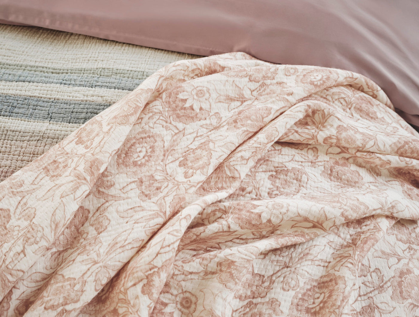 Close-up of Coyuchi Balboa Matelassé throw draped over bed, blush floral print on ivory cotton.