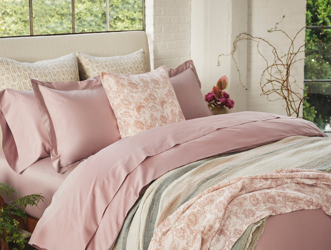 Blush duvet and floral-print throw layered on a bed with botanical décor.