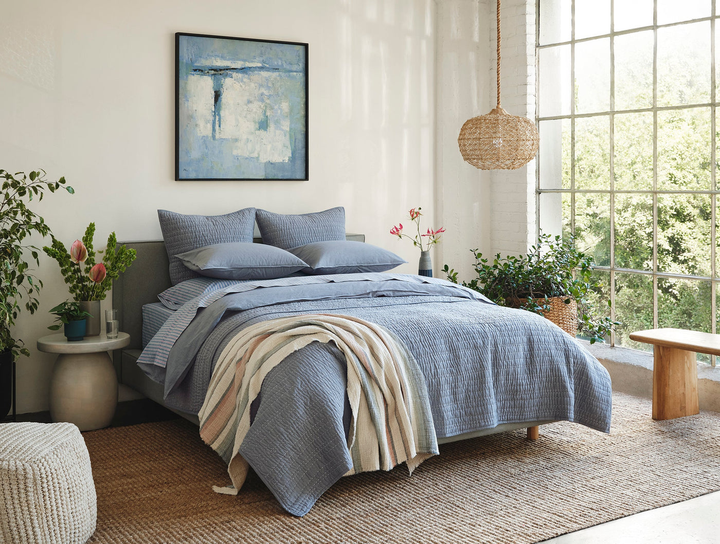Coyuchi Crinkled Percale sheet set styled on bed in blue, with natural throw and botanical accents.