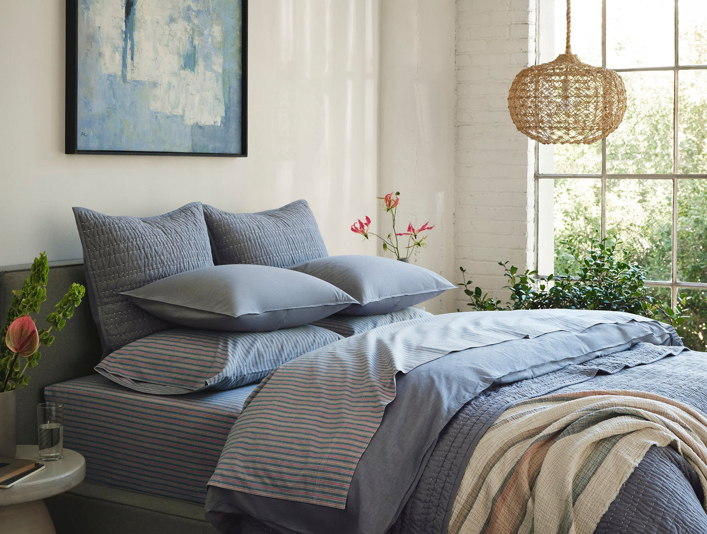 Close-up of Coyuchi Crinkled Percale sham in slate blue, styled on a layered bed with striped bedding.