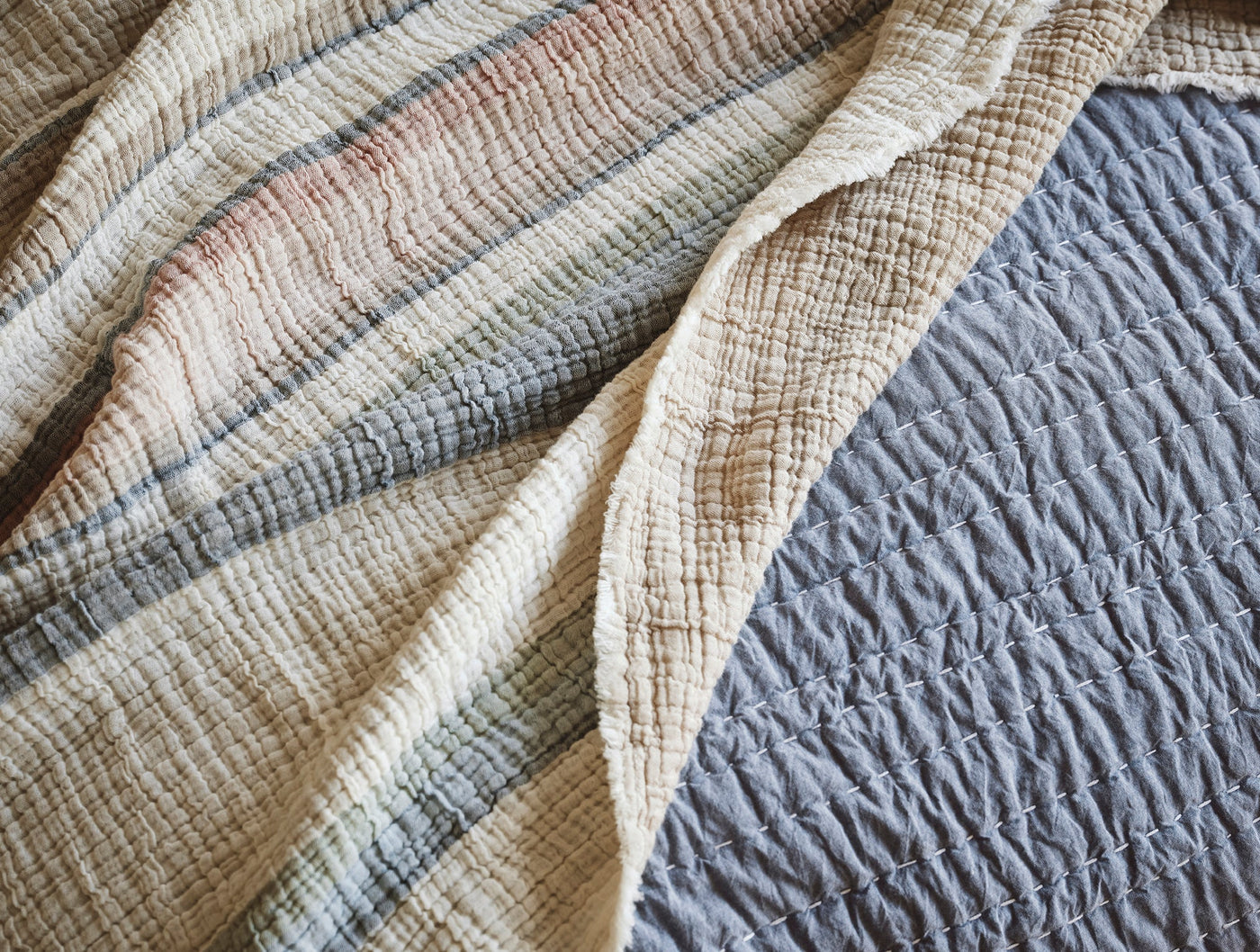 Close-up of Coyuchi Topanga Matelassé blanket reverse in natural stripe beside slate quilted texture.