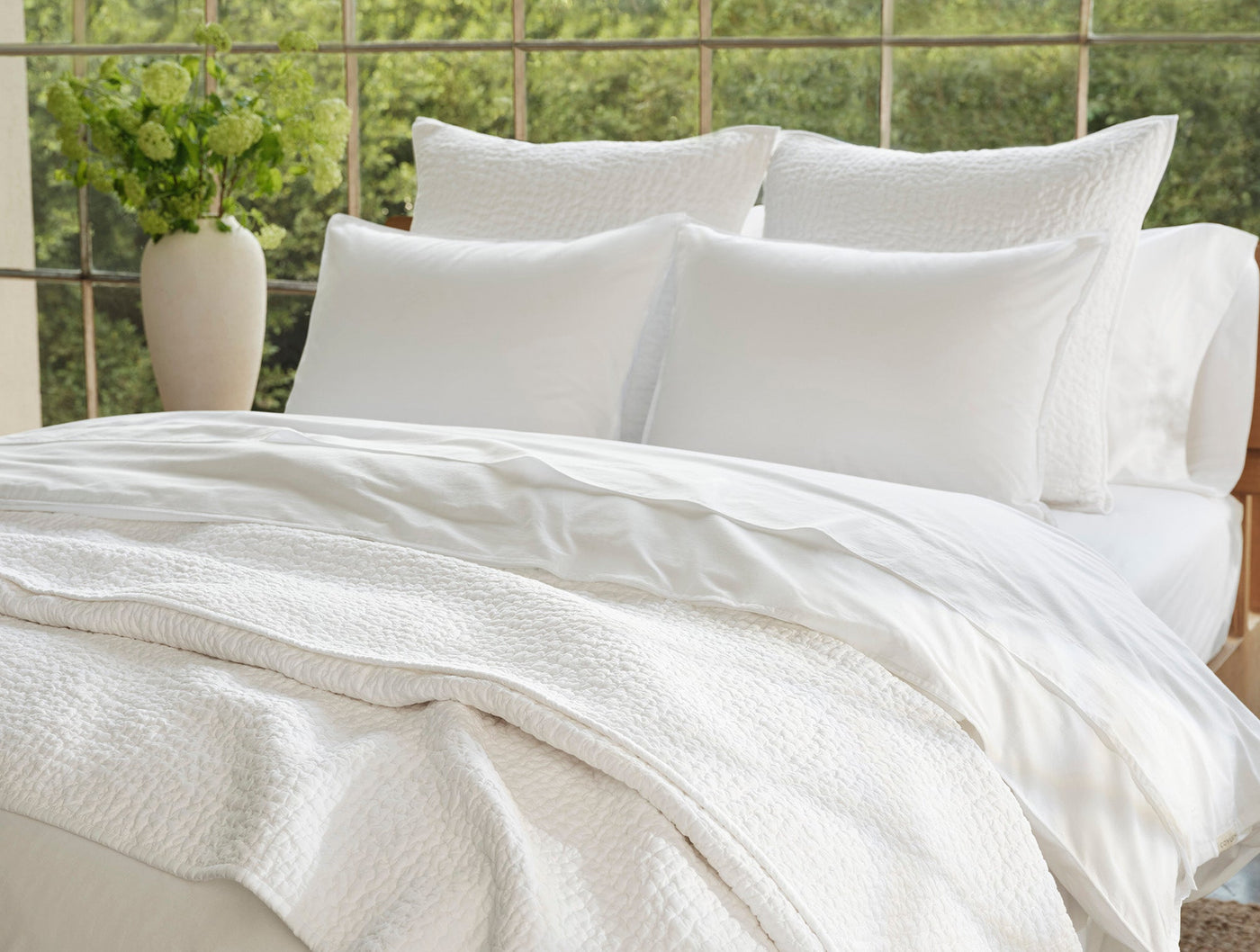 Close-up of white crinkled percale pillow sham styled on a bed with layered bedding.