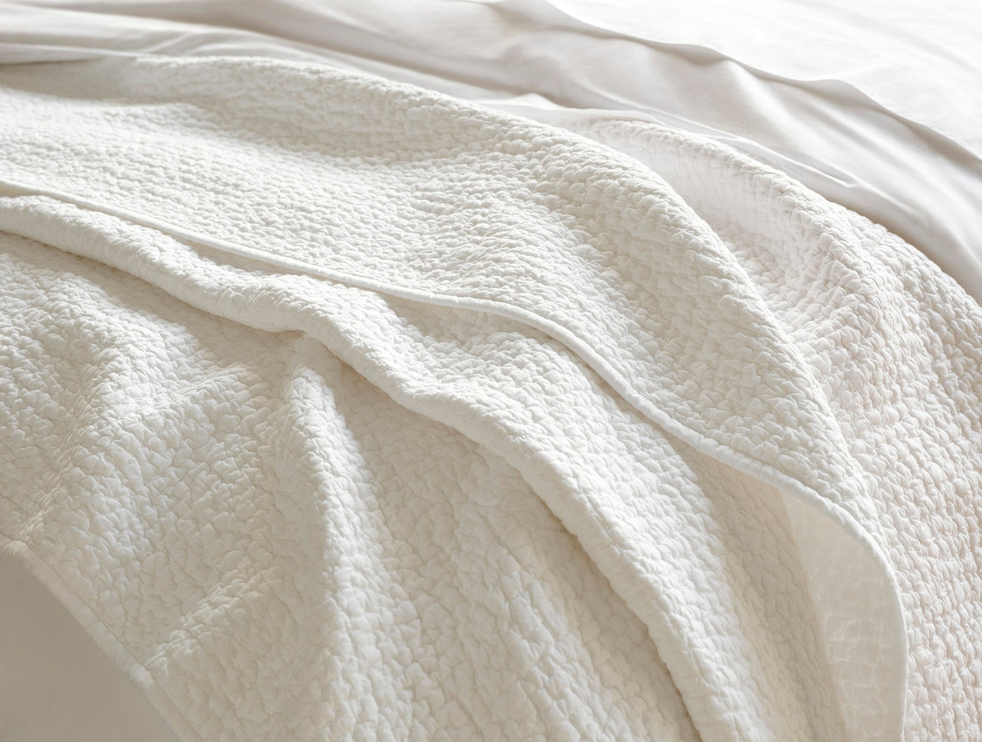Close-up of ivory Coyuchi quilt showing pebbled texture and handstitched detail draped over bed.