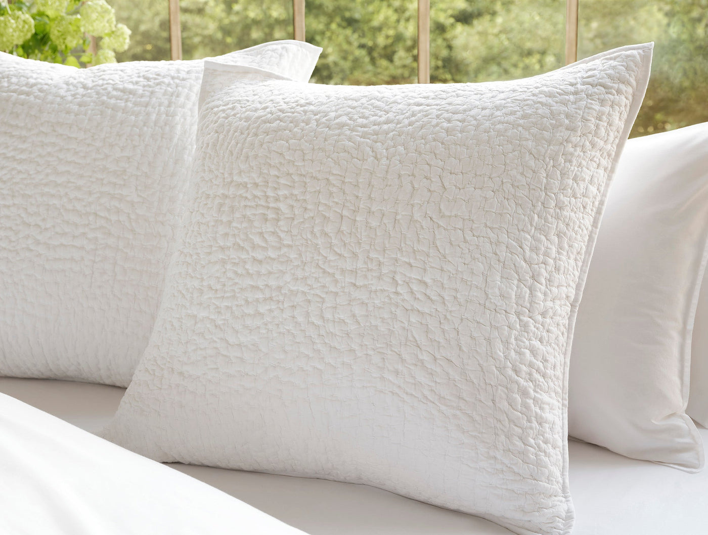 Two white Coyuchi Pebbled Handstitched shams showing organic quilted texture, styled on a bed.