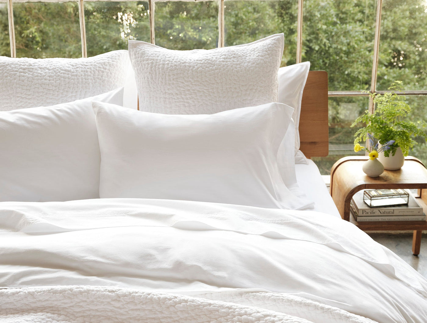 Coyuchi Crinkled Percale pillowcases in white styled on a made bed, garden view.