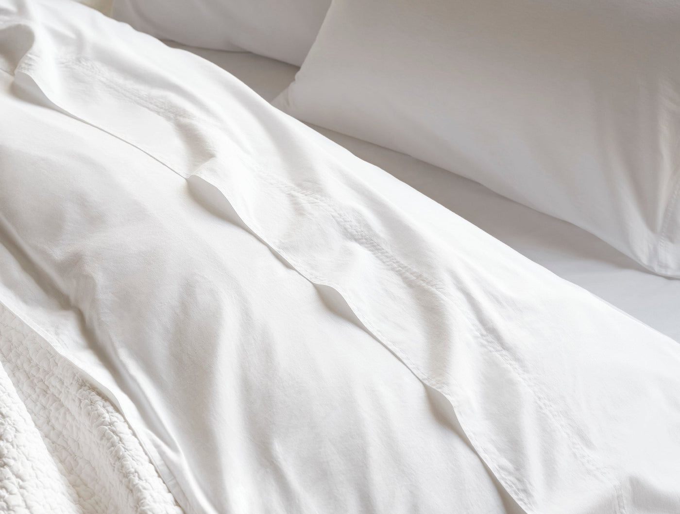 White crinkled percale duvet cover draped on a bed with pillow, natural light.