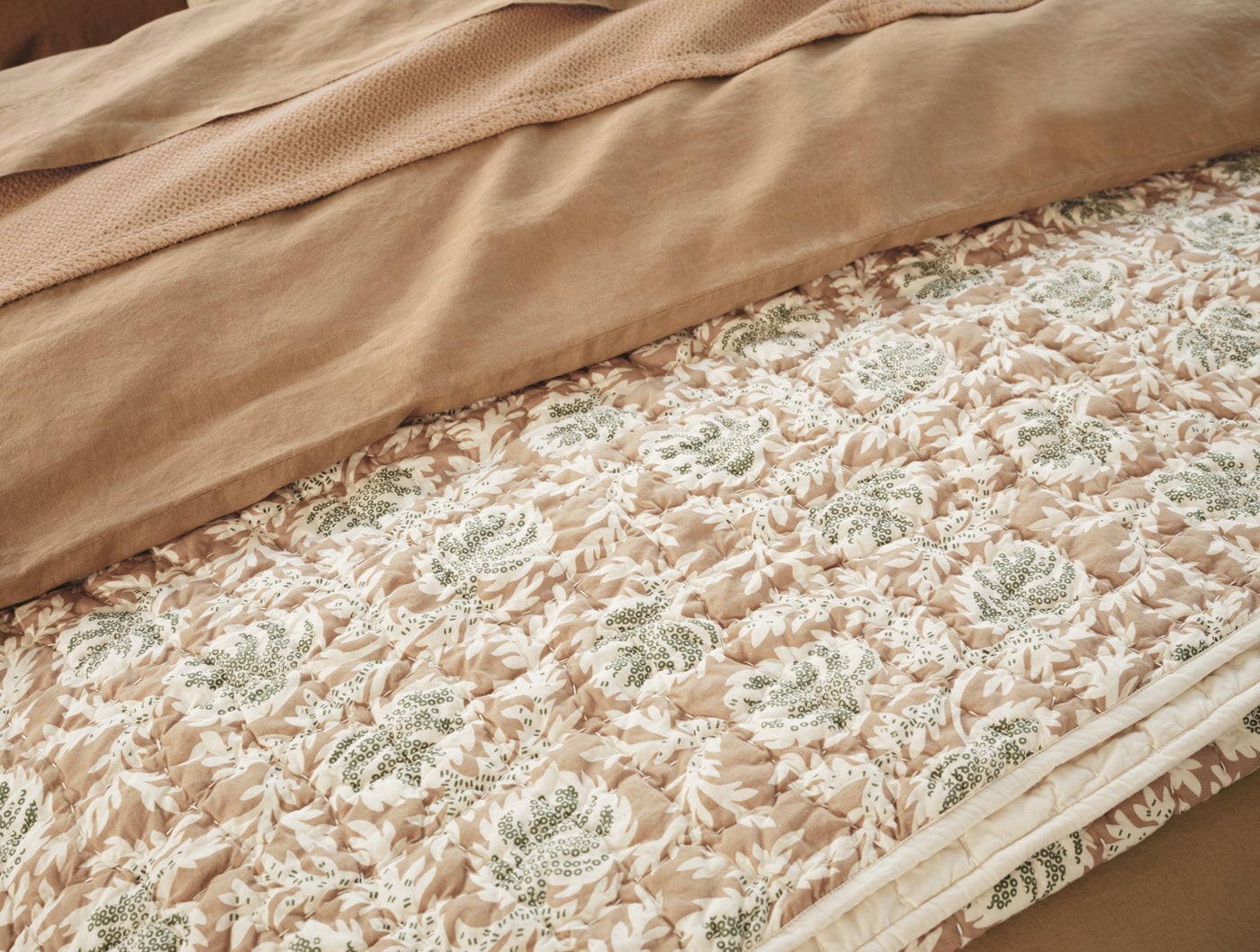 Close-up of Coyuchi Robles quilt's ivory and sage floral block-print pattern with handstitched detail.