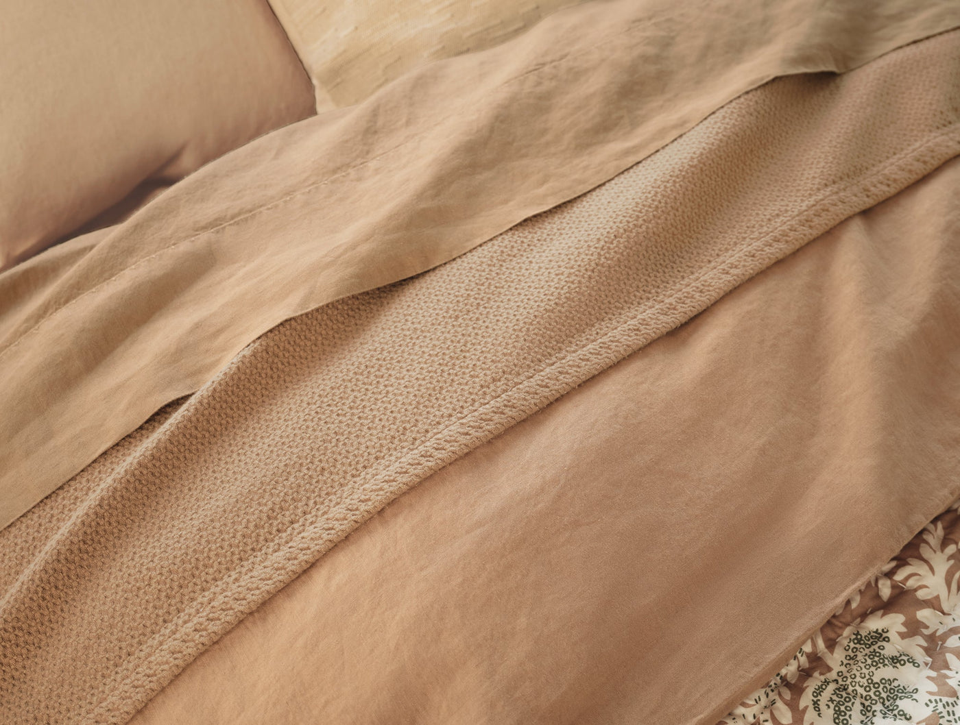 Close-up of camel linen fitted sheet hem detail showing textured weave against draped bedding.
