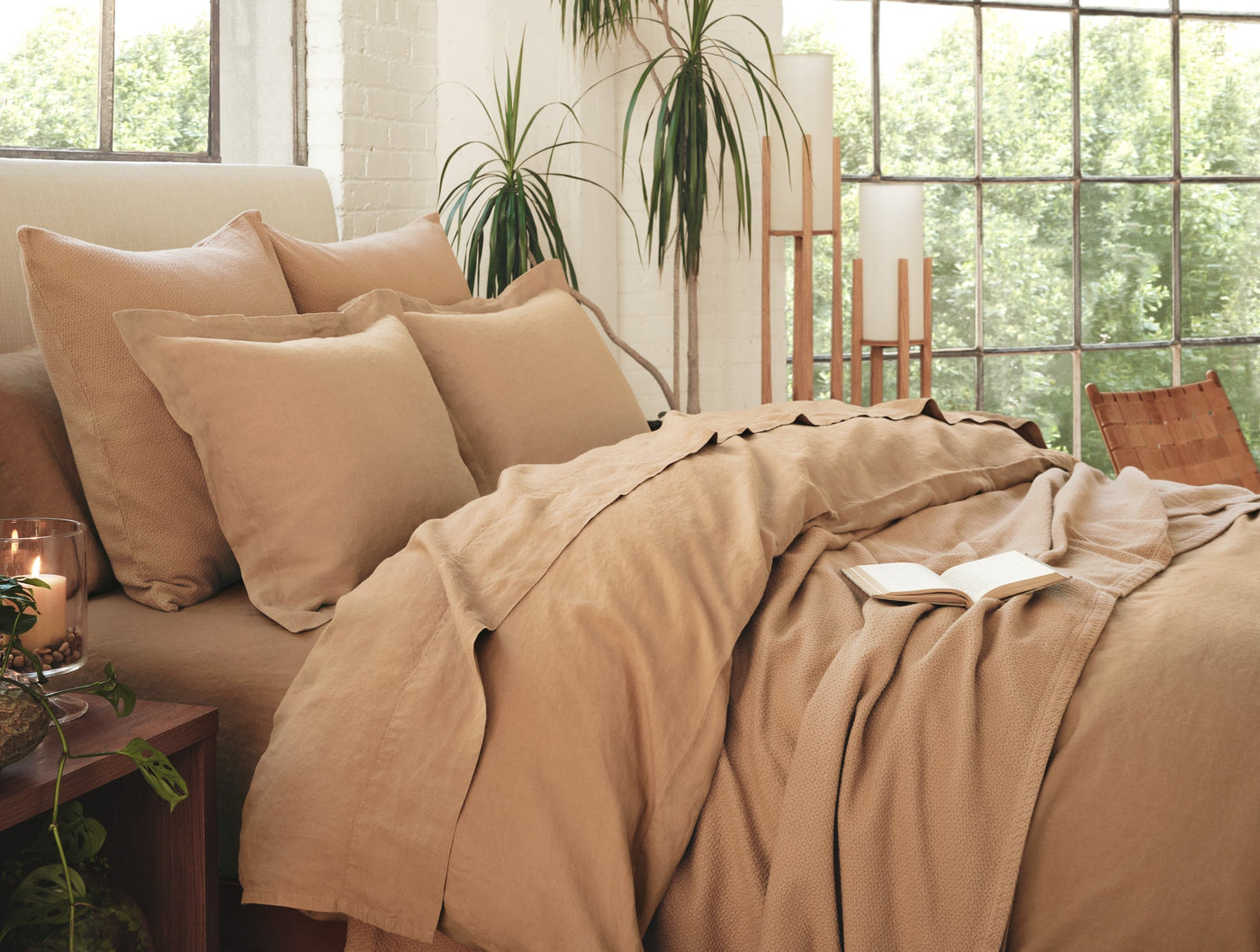 Coyuchi Relaxed Linen duvet cover in camel styled on bed with layered pillows and open book.
