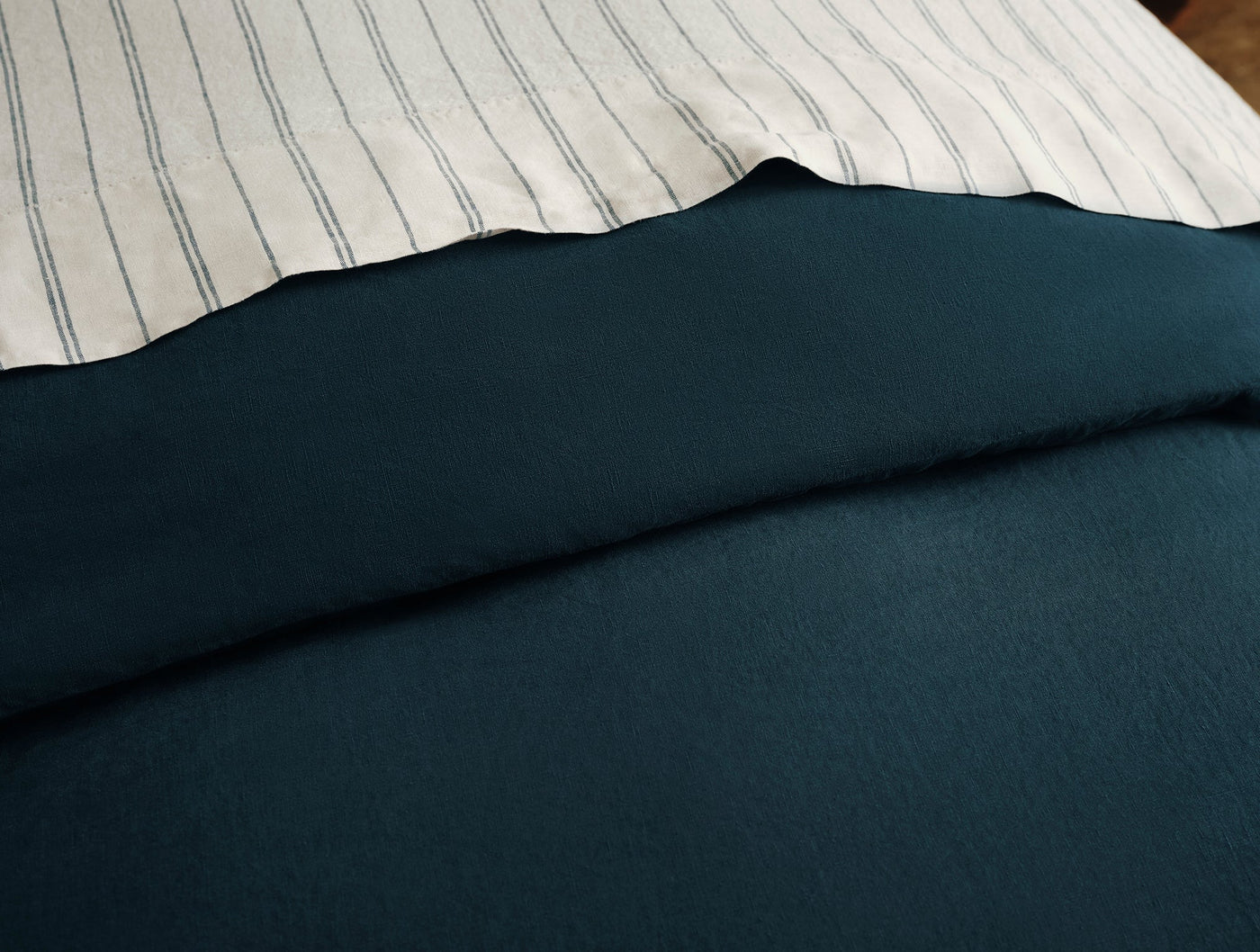 Navy linen duvet cover folded back revealing ivory striped sheet beneath.