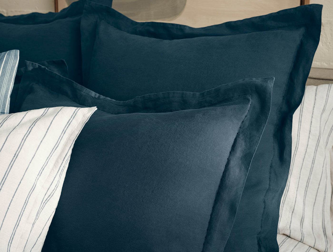 Deep navy linen sham with flanged border, styled with white striped pillows on a bed.