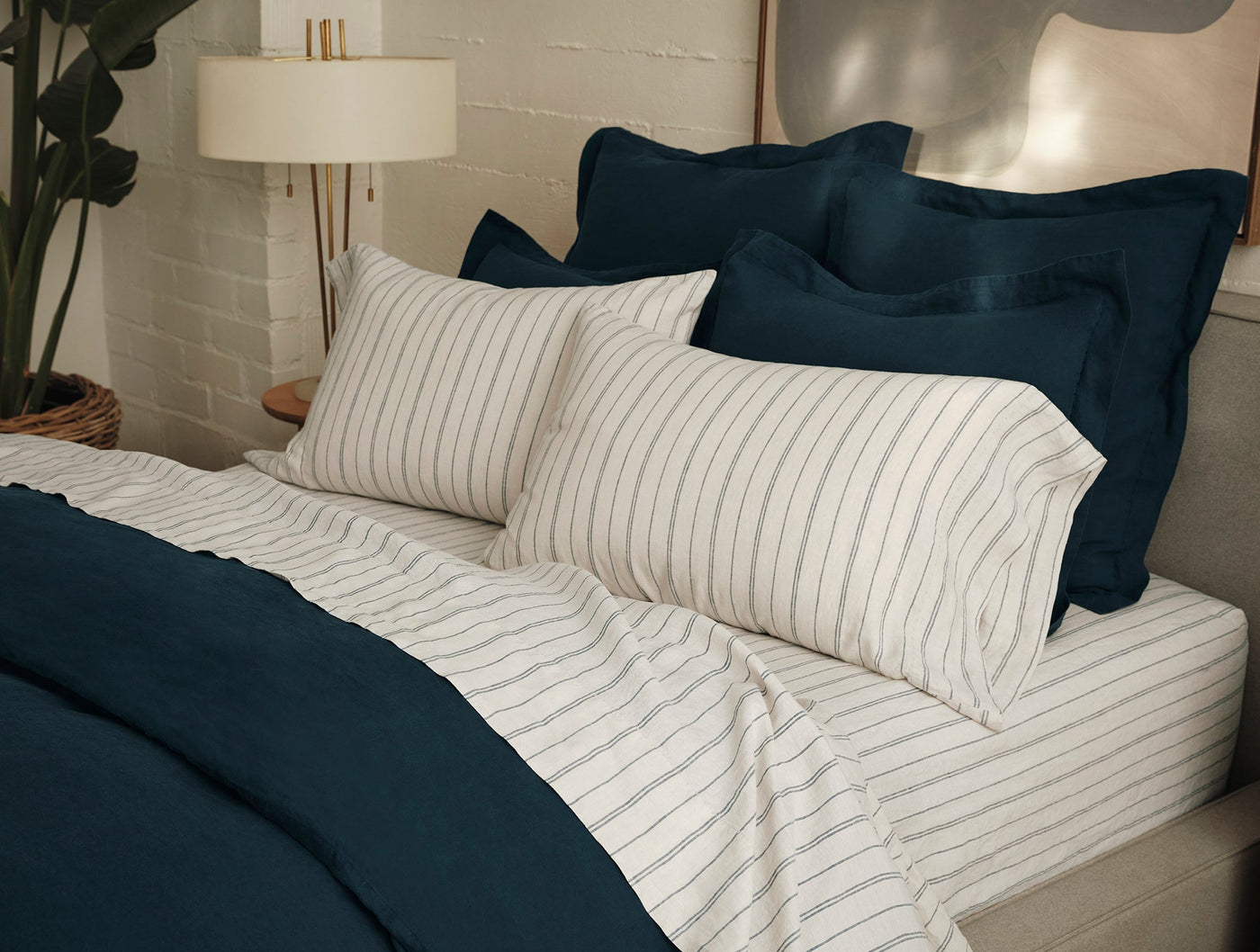 Ivory striped linen sheet set styled with teal duvet, close view of pillowcases on bed.
