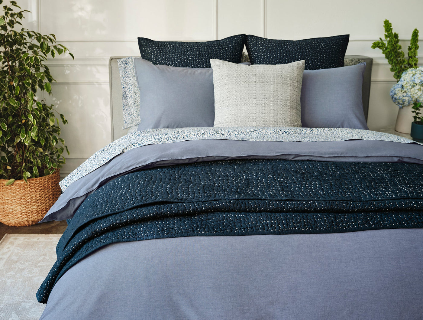 Navy blue Coyuchi Pebbled Handstitched quilt draped across a styled bed with layered bedding.